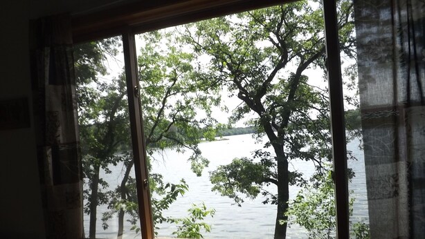 Ein Zimmer mit großem Fenster mit Blick auf ein Gewässer und Bäume.