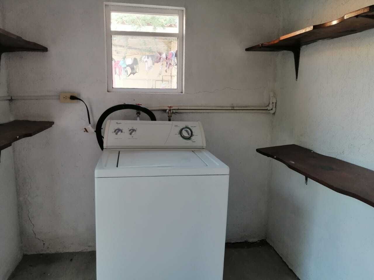 Une petite buanderie équipée d’un lave-linge, d’une fenêtre et d’une étagère en métal.