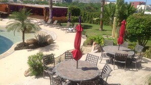Ein Poolbereich eines Resorts mit Liegestühlen und Sonnenschirmen, umgeben von Palmen und viel Grün.