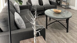 Un salon moderne avec un canapé gris, des coussins à motifs, une table basse en verre et une branche décorative.