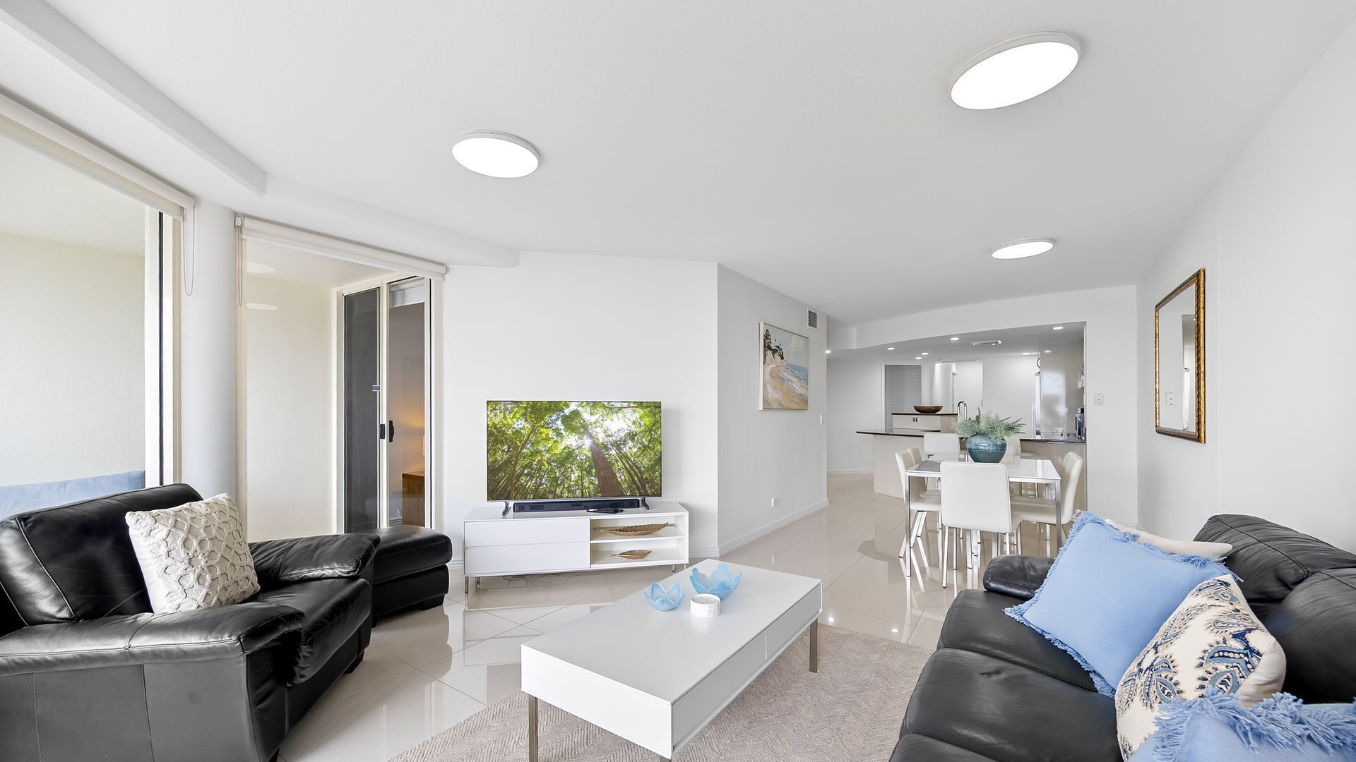 A modern living room with a flat-screen TV, a coffee table, and two sofas.