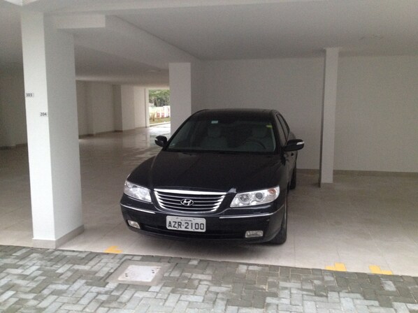Un coche negro estacionado en un garaje con pilares blancos y suelo de baldosas.
