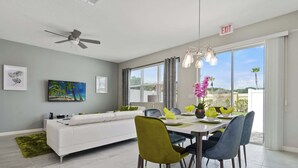 A modern dining area with a white sofa, a dining table with chairs, and a ceiling fan. - Family 4Bd Home Game Room Resort Near Disney 5147 (Kissimmee)