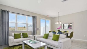 A modern living room with a white sofa, green cushions, a white coffee table, and a large window with curtains. - Family 4Bd Home Game Room Resort Near Disney 5147 (Kissimmee)
