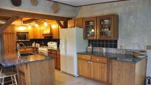 A kitchen with wooden cabinets, a central island, a refrigerator, and a microwave. - Private Post & Beam Home Ideal for Family or Group Gatherings (Killington)