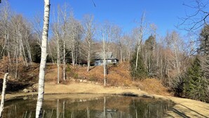 A pond surrounded by birch trees, a small house, and a clear blue sky. - Private Post & Beam Home Ideal for Family or Group Gatherings (Killington)
