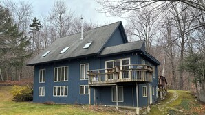 A two-story house with a balcony, a chimney, and a pathway leading to a wooden deck. - Private Post & Beam Home Ideal for Family or Group Gatherings (Killington)