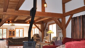 A spacious loft with exposed wooden beams, a fireplace, and a cozy seating area with a red sofa and a patterned armchair. - Private Post & Beam Home Ideal for Family or Group Gatherings (Killington)