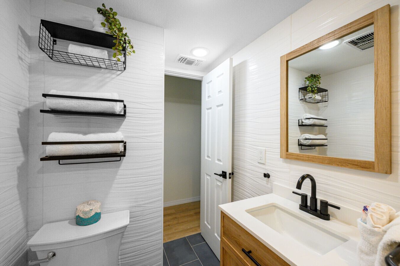 A bathroom with a toilet, towel racks, a sink with a mirror, and a door leading to another room.