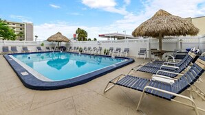 Una piscina con sillas de descanso y sombrillas de paja.
