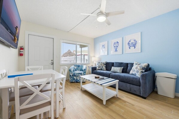 A living room with a blue sofa, white chairs, a coffee table, and a ceiling fan. - Updated 1 BR Madeira Beach Condo I Pool I Sleeps 5 I Ground Floor (Madeira Beach)