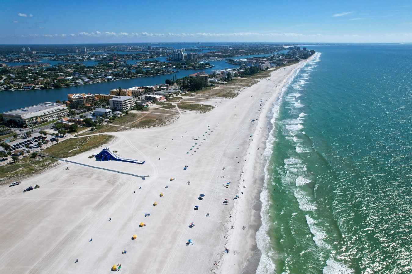 A beach with a water slide, a long stretch of sand, and a view of the ocean.