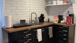 A modern kitchen with white subway tiles, a wooden countertop, black cabinets, and a blue trash bin. - Launchpad~3 Beds,  Rain Shower, Top Golf NearBy (Thornton)