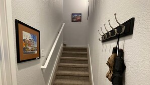 A carpeted staircase with a white railing, a coat rack with jackets, and a framed picture on the wall. - Launchpad~3 Beds,  Rain Shower, Top Golf NearBy (Thornton)