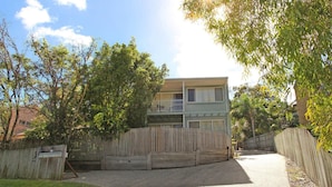 A two-story residential building with a balcony, surrounded by a wooden fence and trees. - Toorumbee 4/38 - Three Bedroom Townhouse Pet Friendly on Request* (Mooloolaba)
