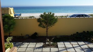 Une vue d’une plage avec un ciel dégagé, une voiture garée sur la plage et un mur jaune au premier plan.