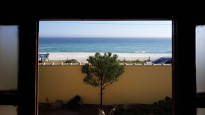 Une vue à travers une fenêtre sur une plage, avec un ciel dégagé, du sable et quelques arbres.
