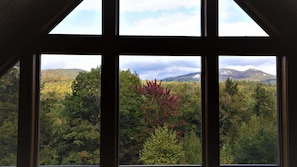 A room with large windows offering a view of a forested landscape with hills.