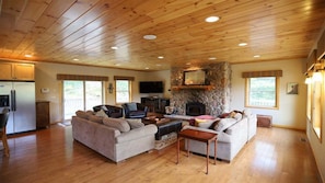 A spacious living room with a stone fireplace, wooden ceiling, and a large TV.