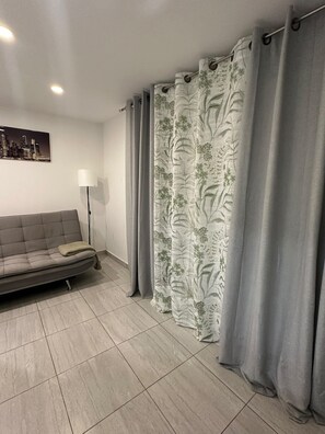 A living room with a grey sofa, a floor lamp, and a curtain with a floral pattern. - REMODELED APARTMENT IN THE CITY CENTER. (FARO) (faro)
