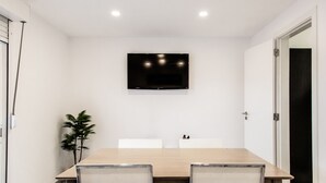A conference room with a long table, chairs, a mounted TV, and a potted plant.
