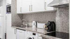 A modern kitchen with white cabinets, a built-in washing machine, a coffee maker, and an oven.