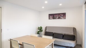 A modern living room with a wooden dining table, two chairs, a sofa with striped cushions, and a cityscape artwork on the wall.