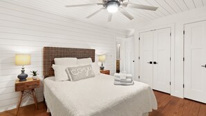 A bedroom with a bed, two bedside tables, a ceiling fan, and white doors.