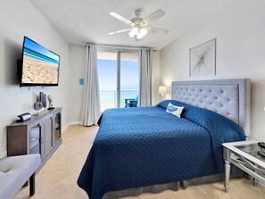 A hotel room with a bed, a desk, a television, a ceiling fan, and a view of the ocean. - Stressless Retreat 3 Bedrooms | 2 Bathrooms |Pure Relaxation & Beach Service with 2 chairs and an umbrella. (Navarre Beach)