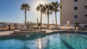 Una piscina amb gandules, palmeres i un edifici al fons.