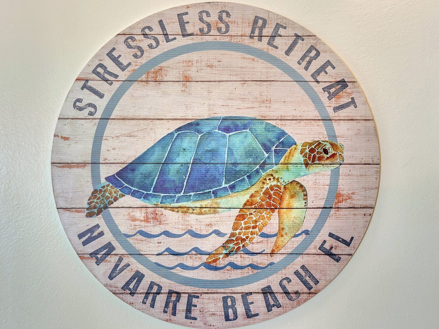 En rund träskylt med en bild av en havssköldpadda och texten: ”STRESSLESS RETREAT NAVARRE BEACH FL”.