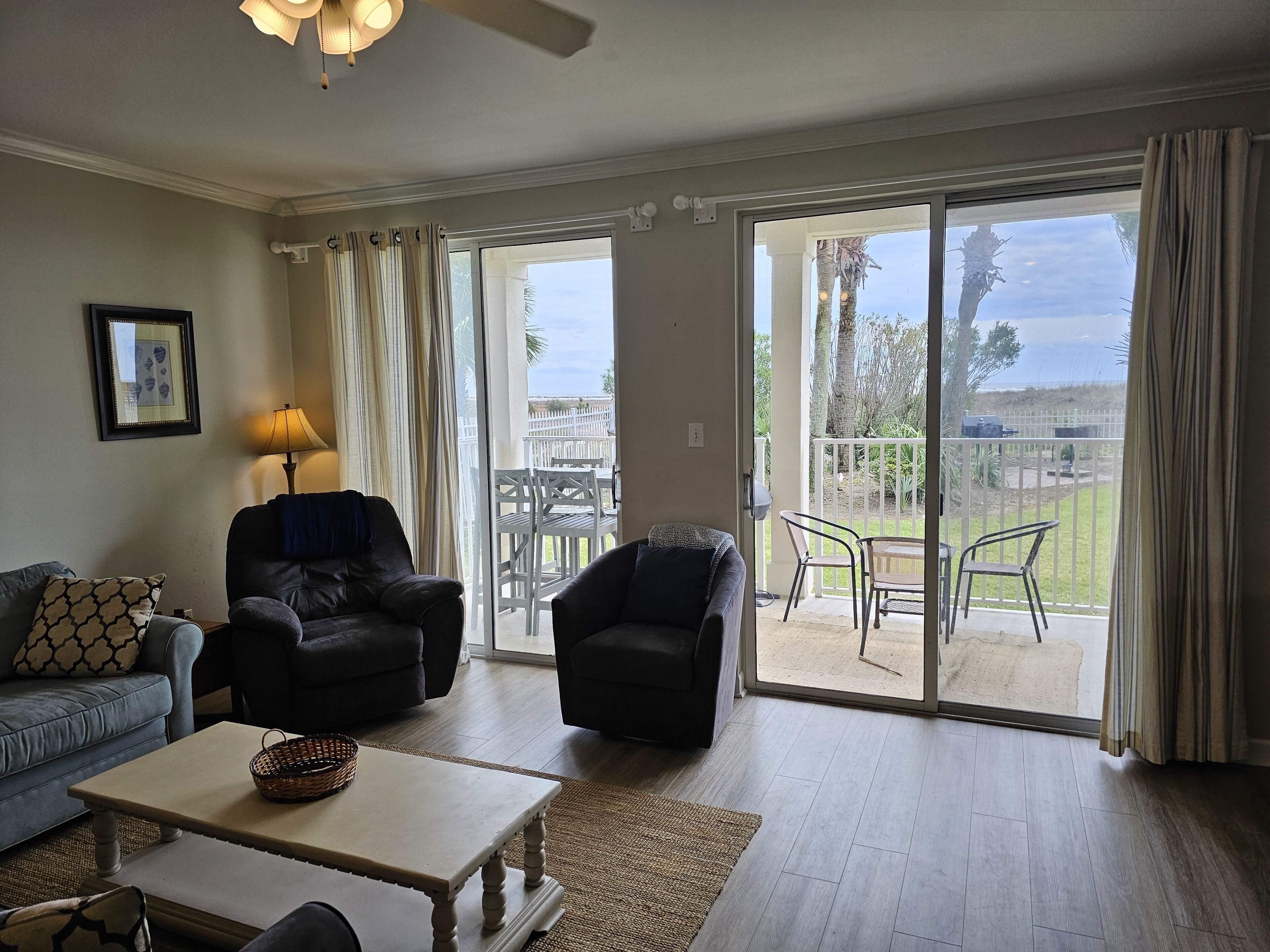 A living room with a sofa, two armchairs, a coffee table, and a view of a fenced outdoor area with chairs and a table.