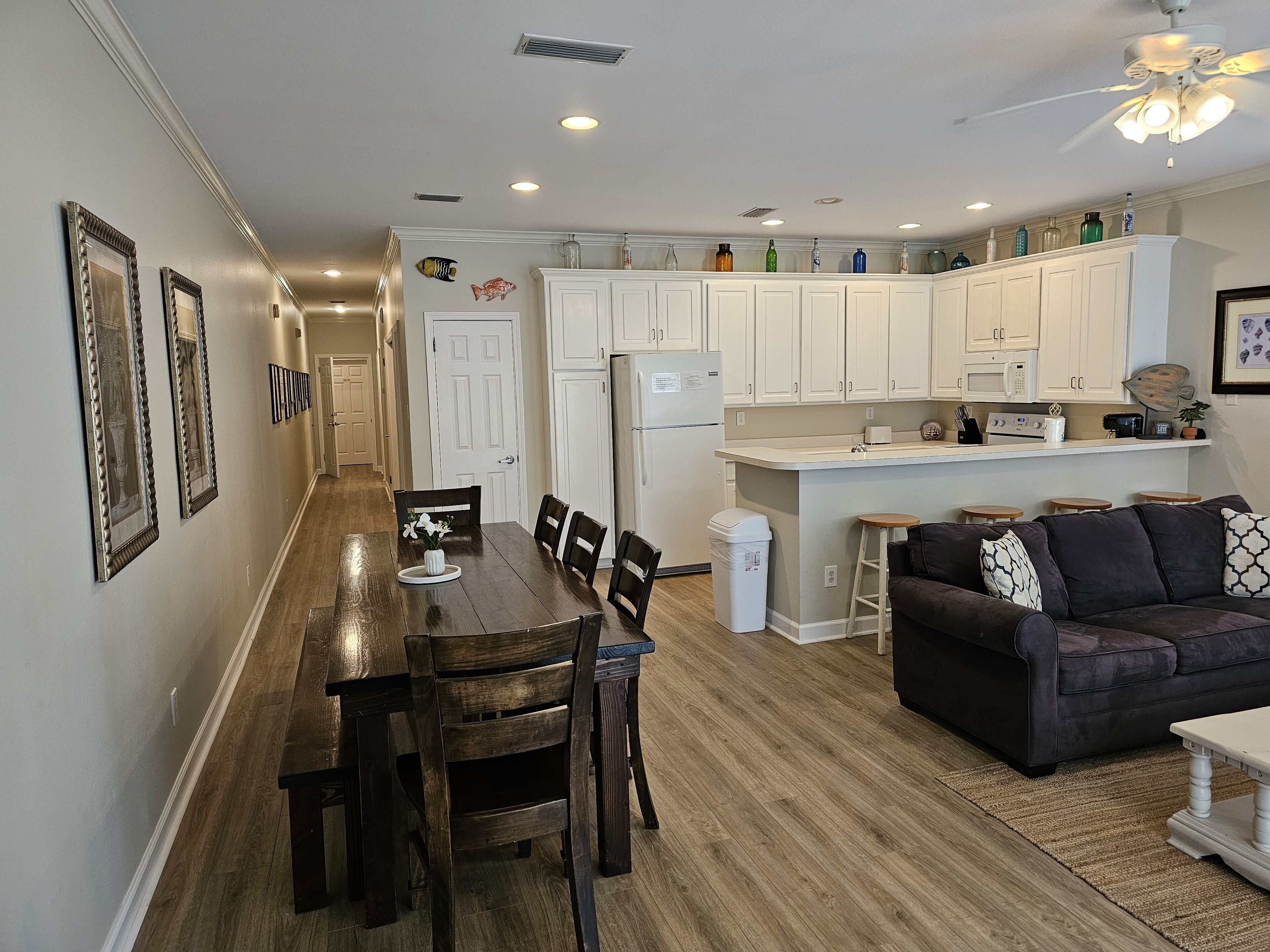 A modern kitchen with white cabinets, a central island, and a dining area with a wooden table and chairs.