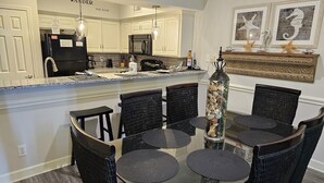 Une cuisine moderne avec des meubles blancs, un réfrigérateur noir et un four à micro-ondes. On y trouve une table à manger avec des chaises noires et un centre de table en verre.