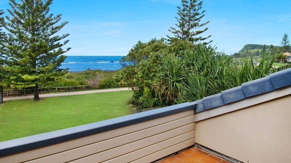 A balcony with a view of the ocean and a grassy lawn.