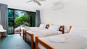 Une chambre d’hôtel avec deux lits en bois, un ventilateur de plafond et une grande fenêtre avec des rideaux.