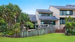Une maison moderne à deux étages, dotée d’un toit en tuiles, d’une clôture en bois et d’un jardin bien entretenu où poussent différentes espèces de plantes.