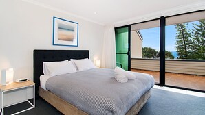 Une chambre moderne avec un grand lit, une table de chevet, un tableau encadré et une vue sur l’extérieur grâce à une porte-fenêtre coulissante.