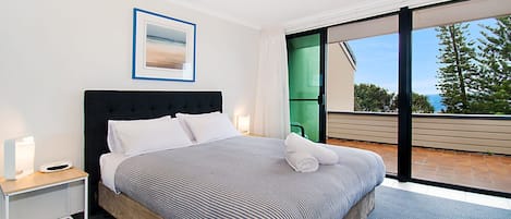 Ein modernes Schlafzimmer mit einem großen Bett, einem Nachttisch, einem gerahmten Bild und Blick ins Freie durch eine Schiebetür.
