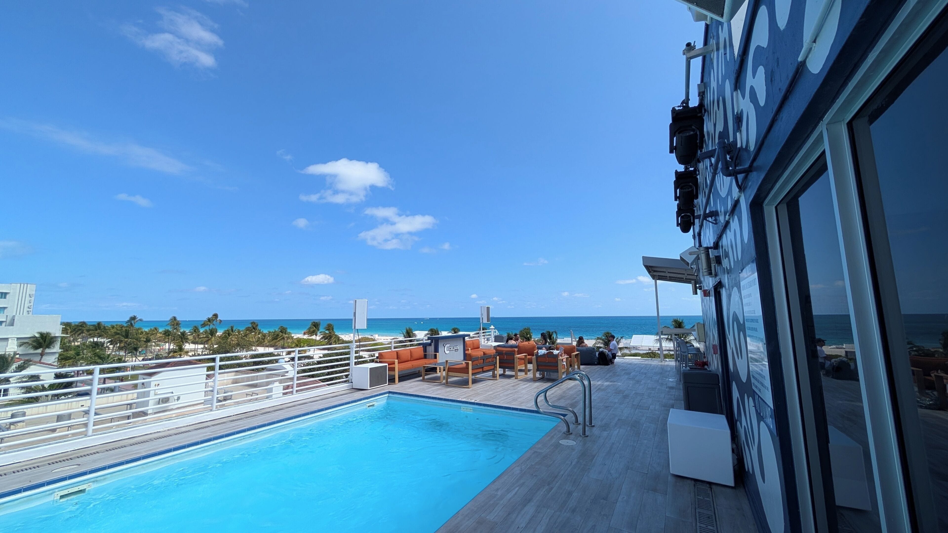 Zona junto a la piscina con vista al océano, mobiliario exterior y un edificio con un ventanal grande.
