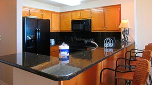 A kitchen with wooden cabinets, a black refrigerator, a microwave, and a coffee maker.