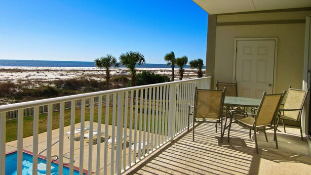 A balcony with a view of the beach, a pool, and outdoor furniture.