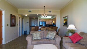 A spacious living room with a beige sofa set, a matching ottoman, and a dining area in the background.