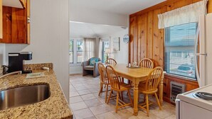 Una cocina con encimeras de granito, un fregadero, armarios de madera, una mesa de comedor con sillas y una ventana con persianas.
