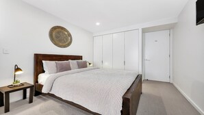 A bedroom with a wooden bed, a bedside table with a lamp, a decorative plate on the wall, and a wardrobe. - THE HARMONY SUITE | WIFI , Short walk to beach | Accom Holidays (TERRIGAL)