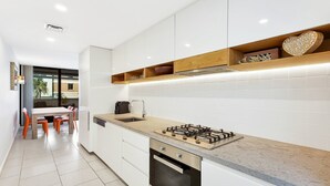 A modern kitchen with white cabinets, a gas stove, and a dining area with orange chairs. - THE HARMONY SUITE | WIFI , Short walk to beach | Accom Holidays (TERRIGAL)