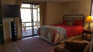 Ein Schlafzimmer mit einem Bett, einem Fernseher, Holzboden, einem roten Teppich und einem Fenster mit Vorhängen.