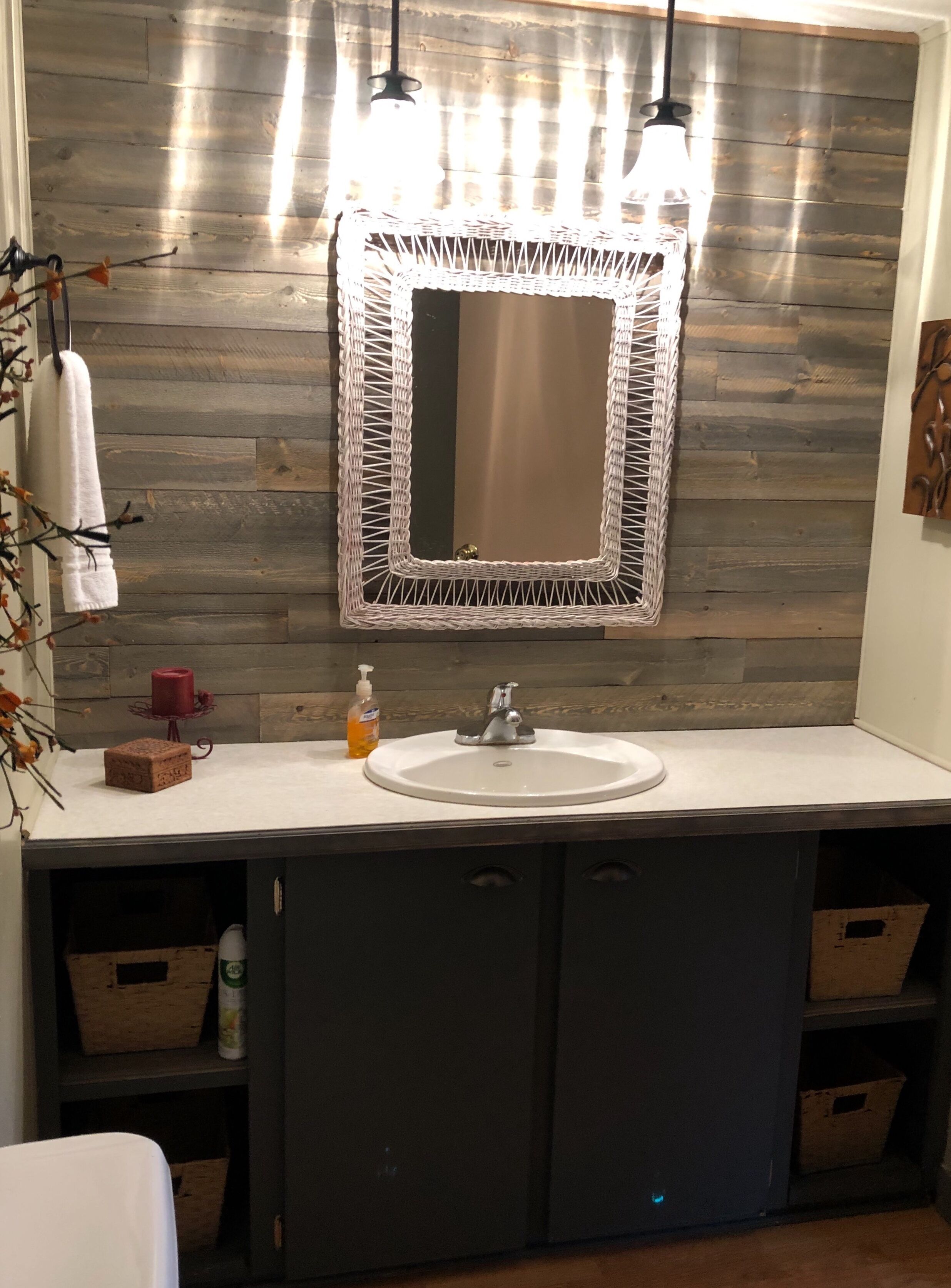 A bathroom with a wooden wall, a round sink, and a mirror with a woven frame.