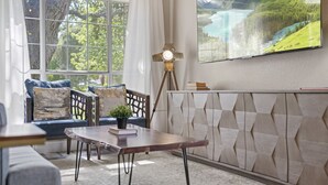 Una sala de estar acogedora con un ventanal grande, una mesa de madera y un televisor montado que muestra un paisaje pintoresco.