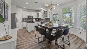 Cocina moderna con armarios blancos, una isla central con taburetes y un ventanal con persianas.